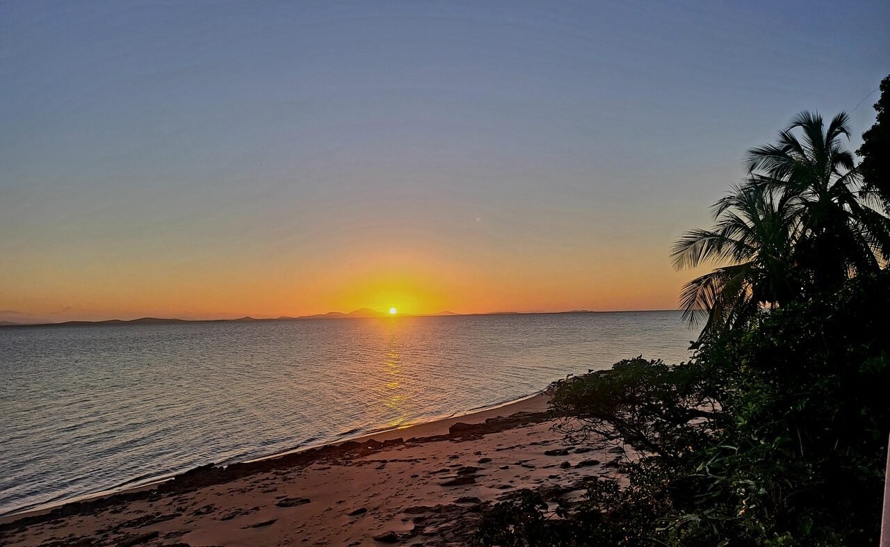 Sunset Scene on Secluded Beach in Australia Beach scene with sunset over calm waters and tropical foliage in silhouette.